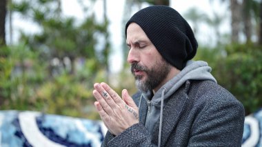 Genç kel adam parkta gözleri kapalı dua ediyor.