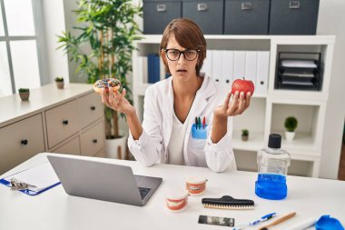 Esmer dişçi kadın şok olmuş suratıyla elma ve çikolatalı çörek tutuyor. Şüpheci ve alaycı görünüyor. 