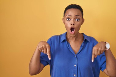 Sarı arka planda dikilen Afro-Amerikalı kadın parmaklarını göstererek reklamını yapıyor, şaşırmış yüz ve ağzını açıyor. 