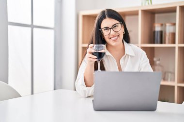 Genç İspanyol kadın dizüstü bilgisayar kullanıyor. Evde şarap içiyor.