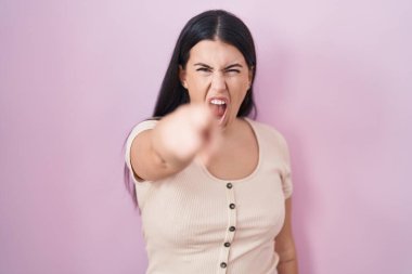 Young hispanic woman standing over pink background pointing displeased and frustrated to the camera, angry and furious with you 