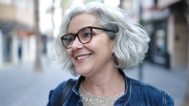 Middle age woman with grey hair smiling confident at street