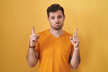 Sarı arka planda dikilen genç İspanyol adam üzgün ve üzgün görünüyor, parmaklarıyla yön gösteriyor, mutsuz ve depresif.. 