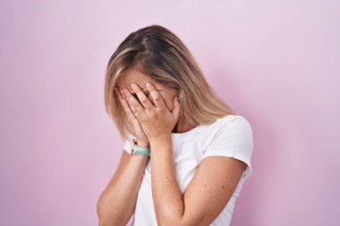 Pembe arka planda duran genç sarışın kadın. Ağlarken suratını ellerle kapatan üzgün bir ifade. depresyon kavramı. 