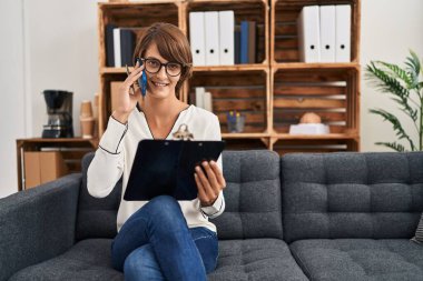 Genç ve güzel İspanyol kadın psikolog psikoloji kliniğinde akıllı telefon okuyarak konuşuyor.