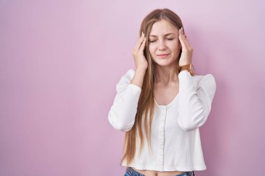 Young caucasian woman standing over pink background with hand on head, headache because stress. suffering migraine. 