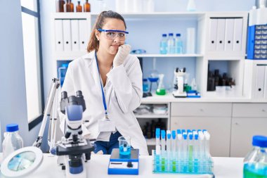 Laboratuvarda çalışan Latin asıllı genç bir kadın gergin ve gergin görünüyor. Ağzı tırnak yiyen ellerle. anksiyete. 