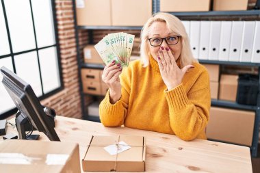 Orta yaşlı beyaz bir kadın küçük işletme şirketinde çalışıyor. Elinde Hong Kong dolarları var. Ağzı elle kapatıyor, şok geçiriyor ve hata yapmaktan korkuyor. şaşırmış ifade 