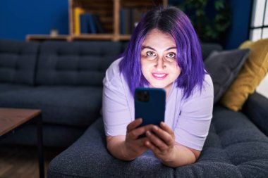 Young beautiful plus size woman using smartphone lying on sofa at home