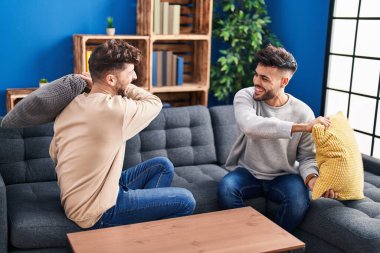 Young couple fighting with cushion sitting on sofa at home
