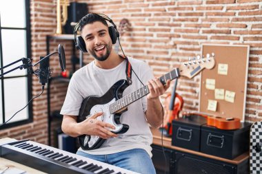 Genç Arap sanatçı müzik stüdyosunda elektro gitar çalarak şarkı söylüyor.