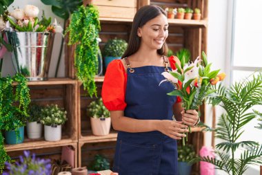 Young beautiful hispanic woman florist holding bouquet of flowers at florist