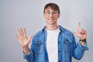 Kafkasyalı sarışın, gözlüklü, yedi numaralı parmaklarıyla işaret eden, kendinden emin ve mutlu bir şekilde gülümseyen adam.. 