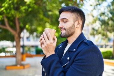 Genç İspanyol adam gülümsüyor. Parkta kahve içiyor.