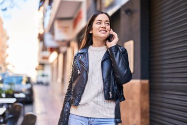 Gülümseyen genç bir kadın caddedeki akıllı telefondan konuşuyor.