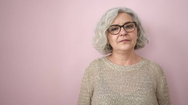 Middle age woman with grey hair standing with serious expression over isolated pink background