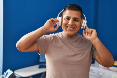 Çamaşır odasında çamaşır makinesi bekleyen müzik dinleyen genç latin adam.