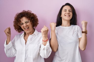 Hispanic mother and daughter wearing casual white t shirt over pink background celebrating surprised and amazed for success with arms raised and eyes closed. winner concept. 