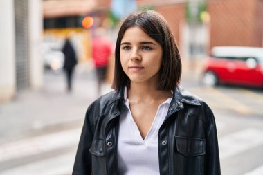 Young beautiful hispanic woman looking to the side with serious expression at street