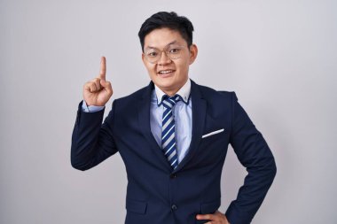 Genç Asyalı takım elbiseli ve kravatlı adam başarılı bir fikirle işaret ediyor. Heyecanlı ve mutlu. Bir numara.. 