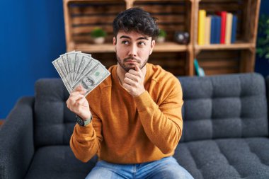 Sakallı, 100 dolarlık banknotlar tutan İspanyol bir adam. Ciddi bir yüz ifadesi var. Çene ve çene üzerine soru soran, kafa karıştırıcı bir fikir. 