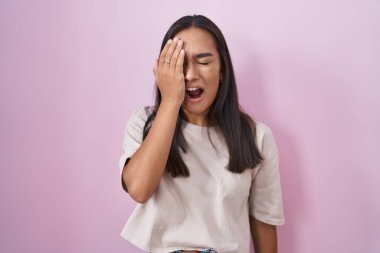 Young hispanic woman standing over pink background yawning tired covering half face, eye and mouth with hand. face hurts in pain. 