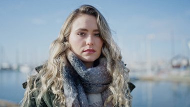 Deniz kenarında ciddi bir ifadeyle duran genç sarışın kadın.