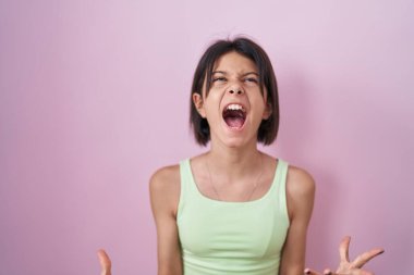 Pembe arka planda duran genç kız çılgın ve kızgın bir şekilde bağırıyor ve agresif bir ifade ve kollarla bağırıyor. hüsran kavramı. 