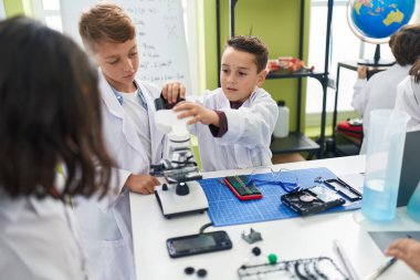 Bir grup öğrenci laboratuvar sınıfında mikroskop kullanarak akıllı telefonu tamir ediyor.