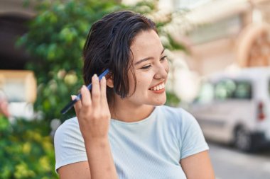 Young hispanic woman smiling confident listening audio message by the smartphone at street