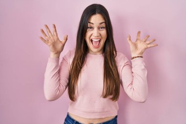 Young brunette woman standing over pink background celebrating crazy and amazed for success with arms raised and open eyes screaming excited. winner concept 