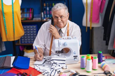 Orta yaşlı, kır saçlı, terzi terzide not defteriyle konuşan akıllı telefon terzisi.