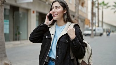 Young beautiful hispanic woman student smiling confident talking on smartphone at street
