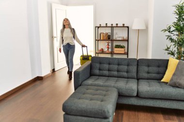 Orta yaşlı, gri saçlı, sırt çantalı bir turist. Elinde bavulla eve gidiyor.