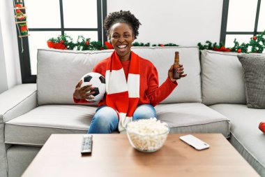 Evdeki kanepede oturan Afrikalı Amerikalı kadın futbol takımını destekliyor.