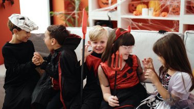 Cadılar Bayramı kostümü giymiş bir grup çocuk evde korku jesti yapıyor.