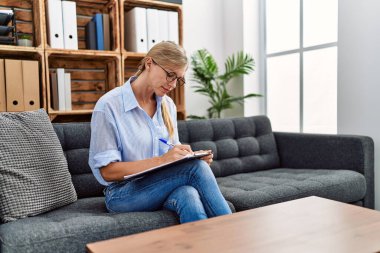 Genç sarışın psikolog, panoya yazı yazıyor klinikteki koltukta oturuyor.