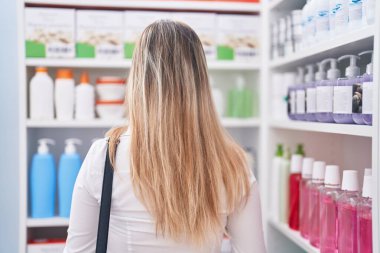 Young blonde woman customer looking shelving at pharmacy