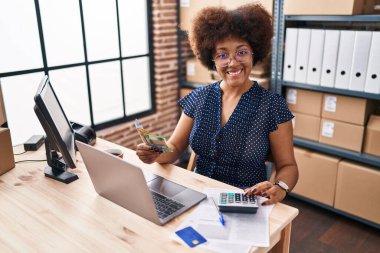 African american woman ecommerce business worker using laptop counting australian dollars at office