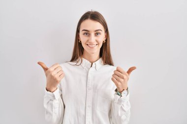 İzole edilmiş arka plan başarı işaretinin başında duran genç beyaz kadın elleriyle olumlu bir jest yapıyor, gülümsüyor ve mutlu. Neşeli ifade ve kazanan jest. 