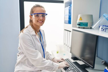 Young blonde woman wearing scientist uniform using computer working at laboratory