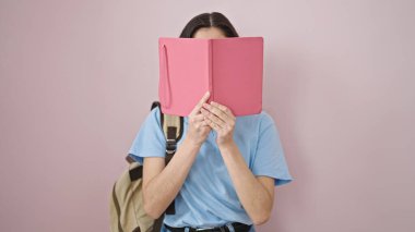 Genç, güzel, İspanyol bir bayan öğrenci, pembe arka planda kitap ile yüzünü kapatıyor.