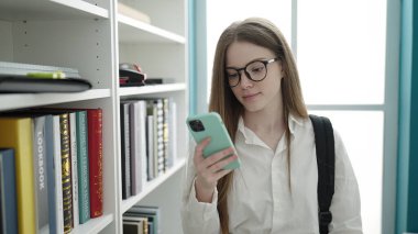 Young blonde woman student using smartphone at university classroom