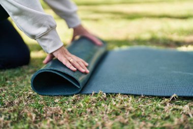 Orta yaşlı bir kadın parkta yoga minderini kapatıyor.