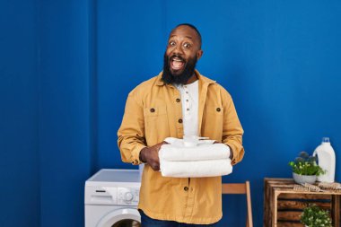 Afrika kökenli Amerikalı adam çamaşır odasında temiz havlu tutuyor. Çılgınlığı kutluyor ve başarıya hayret ediyor. Gözleri açık, heyecanlı bir şekilde bağırıyor.. 