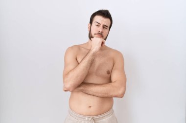 Beyaz arka plan üzerinde tişörtsüz duran genç İspanyol adam kameraya kollarını kavuşturup gülümseyerek ve çenesini kaldırarak bakıyor. Olumlu düşünmek. 