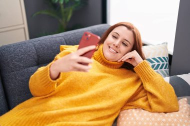 Evdeki kanepede uzanmış akıllı telefon kullanan güzel, iri yarı bir kadın.