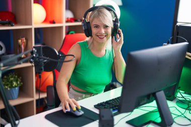 Genç sarışın kadın oyun odasında bilgisayar kullanarak video oyunu oynuyor.