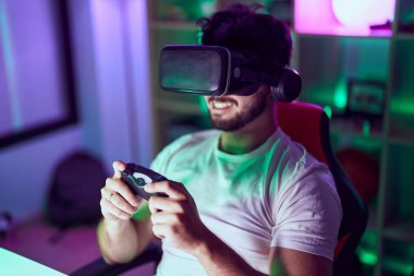 Sanal gerçeklik gözlüğü kullanan İspanyol asıllı genç adam oyun odasında video oyunu oynuyor.