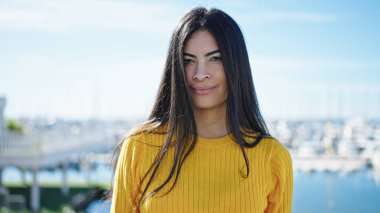 Genç, güzel, İspanyol bir kadın, deniz kenarında sakin bir ifadeyle duruyor.